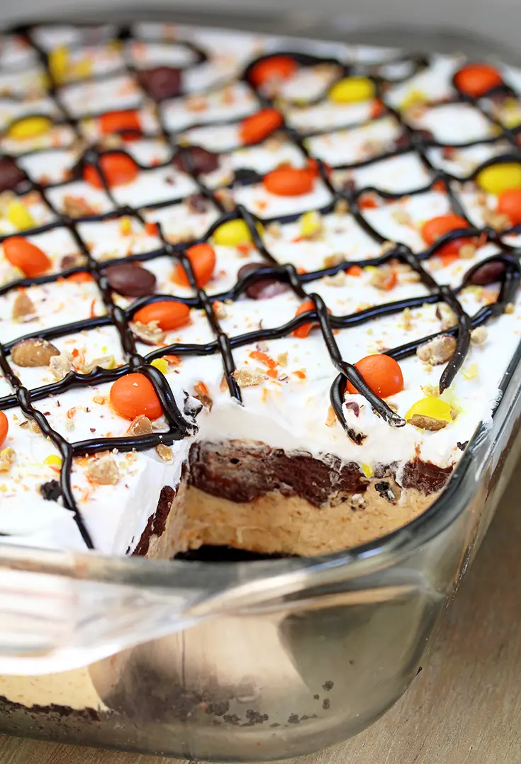 Reese‘s Pieces Peanut Butter Chocolate Lasagna – simple and easy, no bake, layered, rich taste dessert, with Reese‘s pieces, Oreo cookies, peanut butter and chocolate pudding topped with cool whip, Reese‘s pieces, and chocolate syrup.