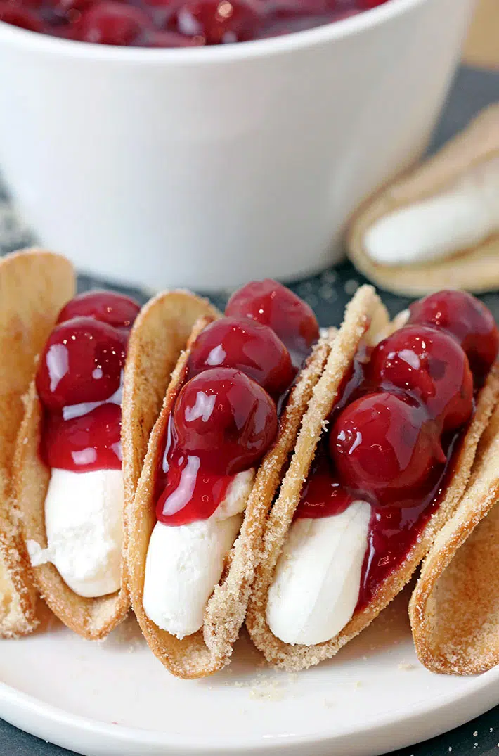 Cherry Cheesecake Tacos – these mini dessert tacos made with sweet ingredients and shaped like traditional tacos are so much fun to prepare, they look classy and are very delicious. You will love crunchy tortilla shells covered with sugar and cinnamon, filled with creamy no bake cheesecake filling that are topped with cherry pie filling.