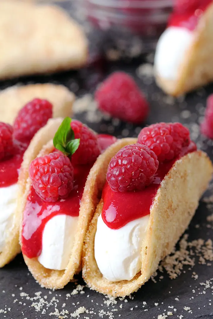 Raspberry Cheesecake Tacos – crunchy tortilla shells, creamy cheesecake filling, topped with raspberry sauce and fresh raspberries on top make this amazing dessert. These incredible bites are perfect for holidays, parties and other events. 