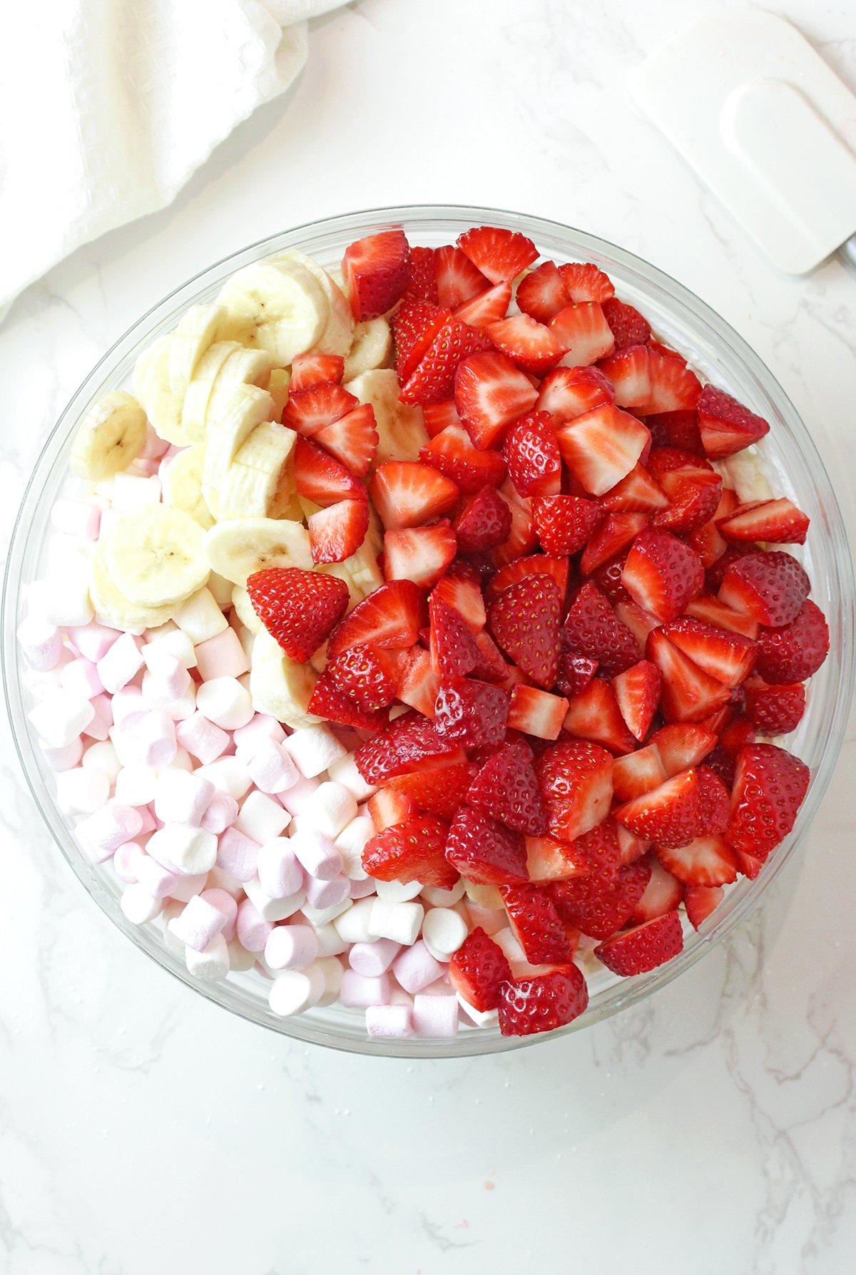 Stirring marshmallows, strawberries, and bananas into fluff salad before serving.