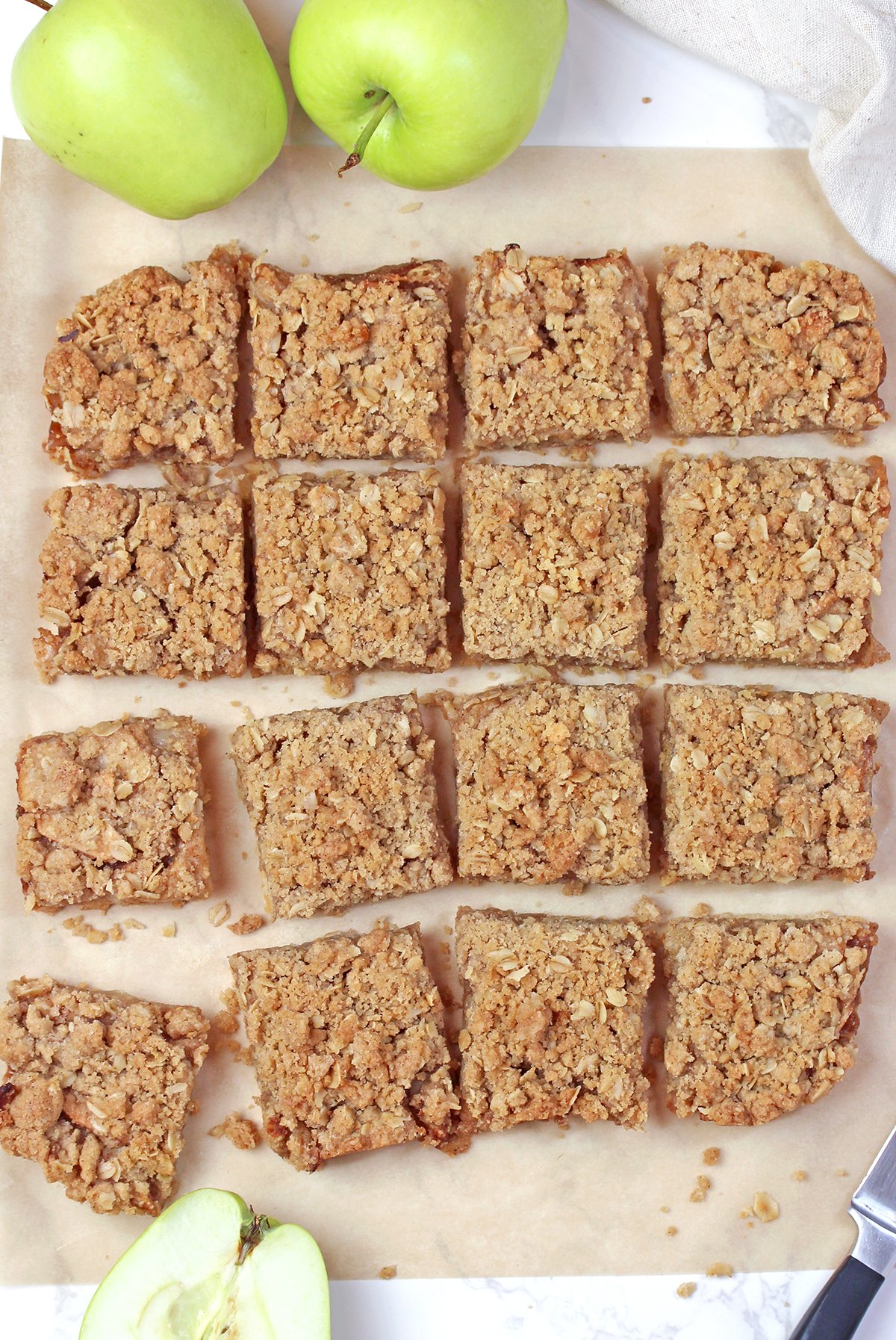 Homemade Apple Crisp Bars sliced into squares and arranged on parchment paper.