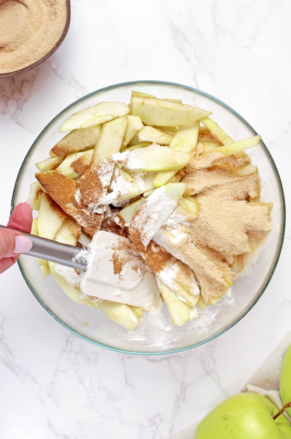 Coating sliced apples with flour, brown sugar, cinnamon, and nutmeg.