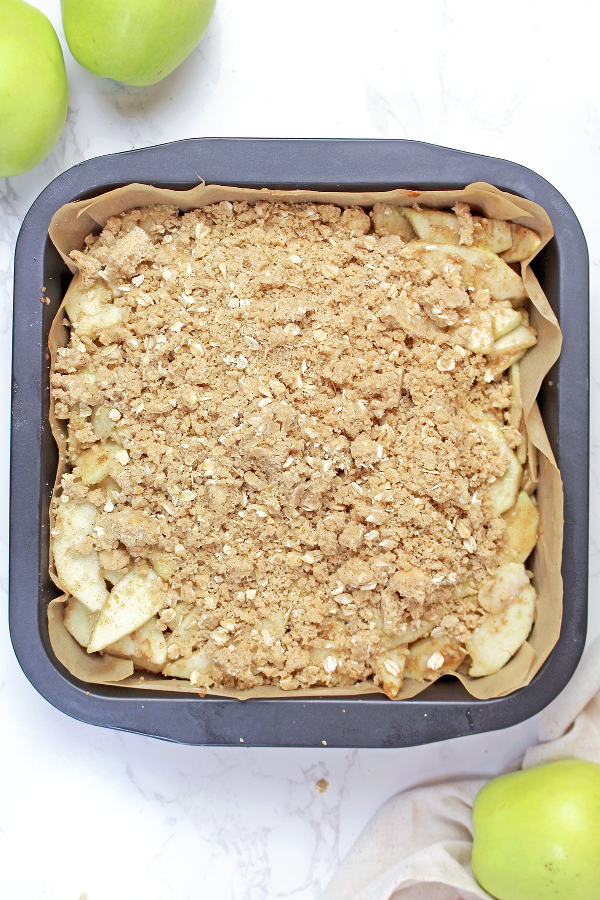 Sprinkling the oat crumble topping evenly over the apple filling.