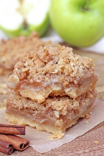 Stacked Apple Crisp Bars with a bite taken out, showing the shortbread crust, apple filling, and oat crumble topping.
