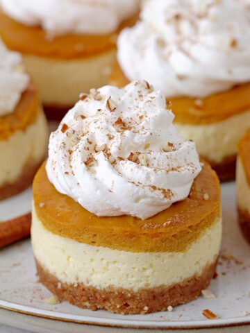 Best Mini Pumpkin Pie Cheesecakes with decadent creamy filling made of cream cheese and pumpkin pie layers on crunchy graham cracker crust, topped with whipped cream are so delicious and yet simple fall dessert, perfect for Thanksgiving.