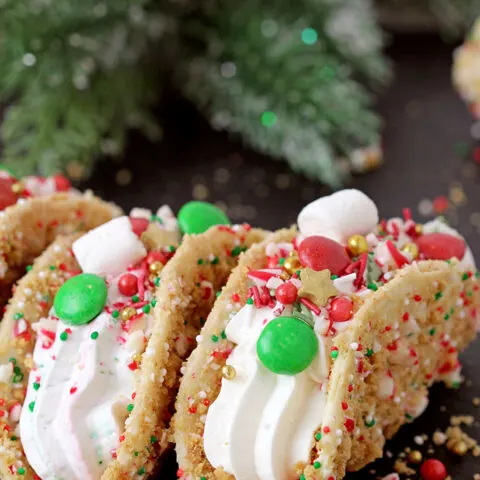 These Christmas Cheesecake Tacos with crunchy graham cracker tortilla shells, rich and creamy cheesecake filling, sprinkled with Christmas sprinkles, M&M's and crushed candy canes is an ultimate dessert you have to try for Christmas 2023!