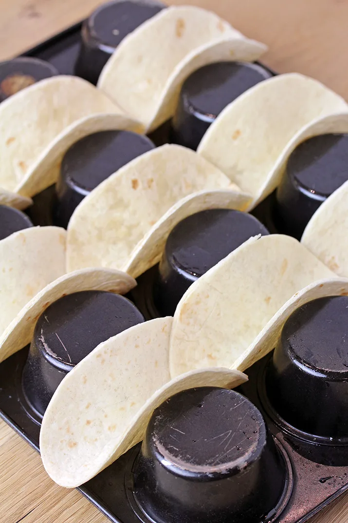 First make taco shells and bake them in the oven, then coat them with white chocolate and crunchy graham cracker crumbs, Christmas sprinkles and crushed candy canes.