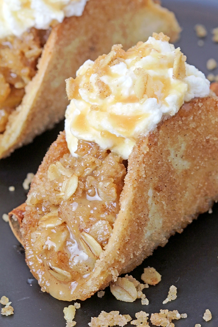 These Apple Crisp Tacos are the ultimate fall dessert, made with crispy cinnamon - sugar tortilla shells filled with apple crisp, topped with whipped topping or ice cream and drizzled with caramel sauce. They are perfect for gatherings, parties, picnics or even holidays.