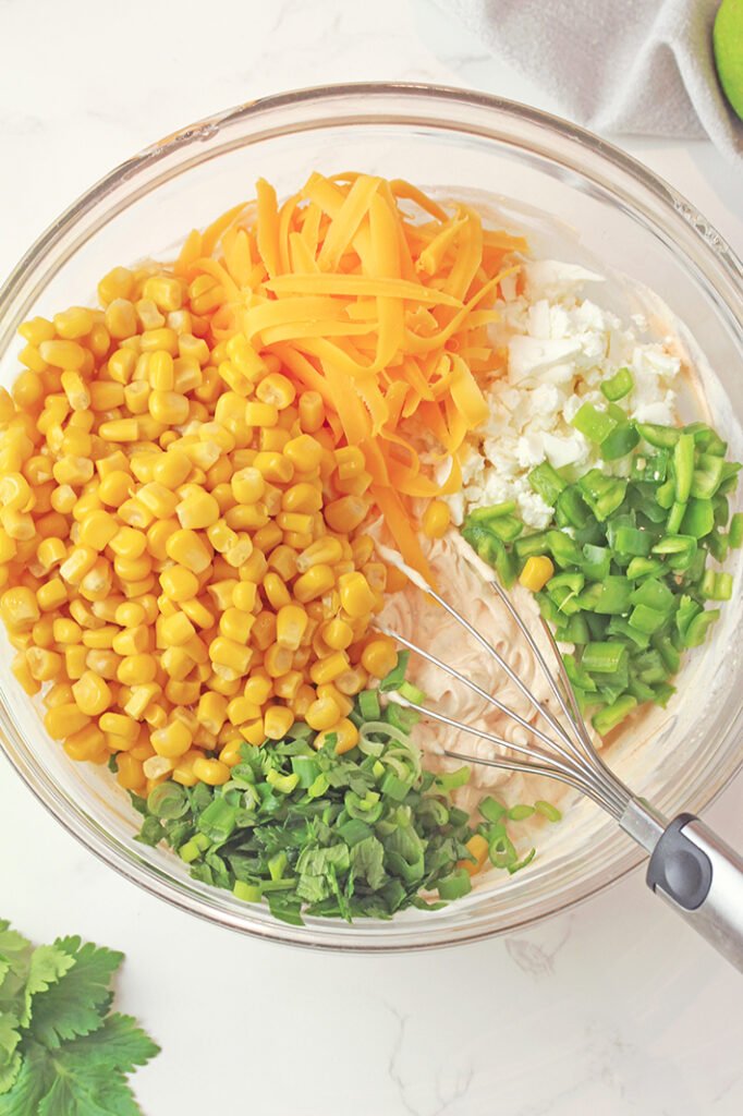 Fold in corn, jalapeño, ½ cup shredded cheddar, cotija or feta cheese, green onions, and cilantro.