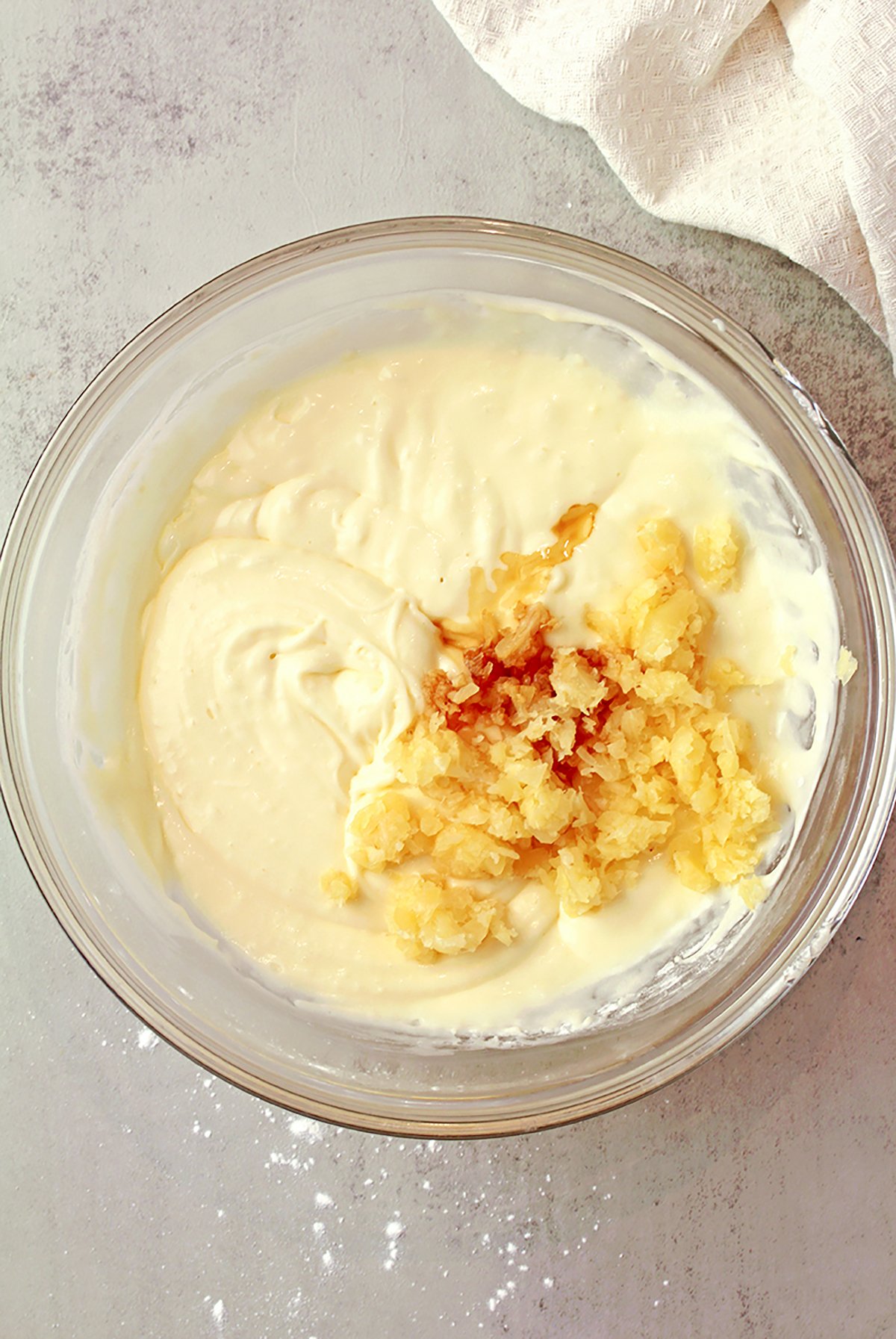 Adding crushed pineapple to cream cheese frosting mixture.
