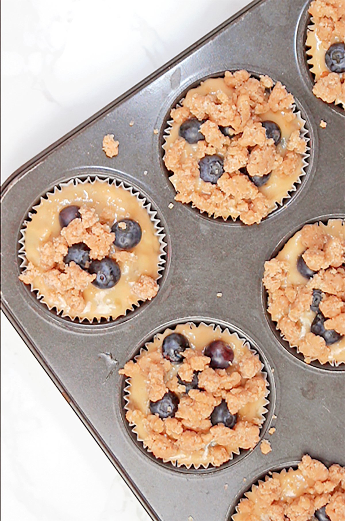 Step 6. Fill the Muffin Tin
Divide the batter evenly among the muffin cups, filling them almost to the top. Add a few extra blueberries on top, then generously sprinkle with the chilled crumb topping.