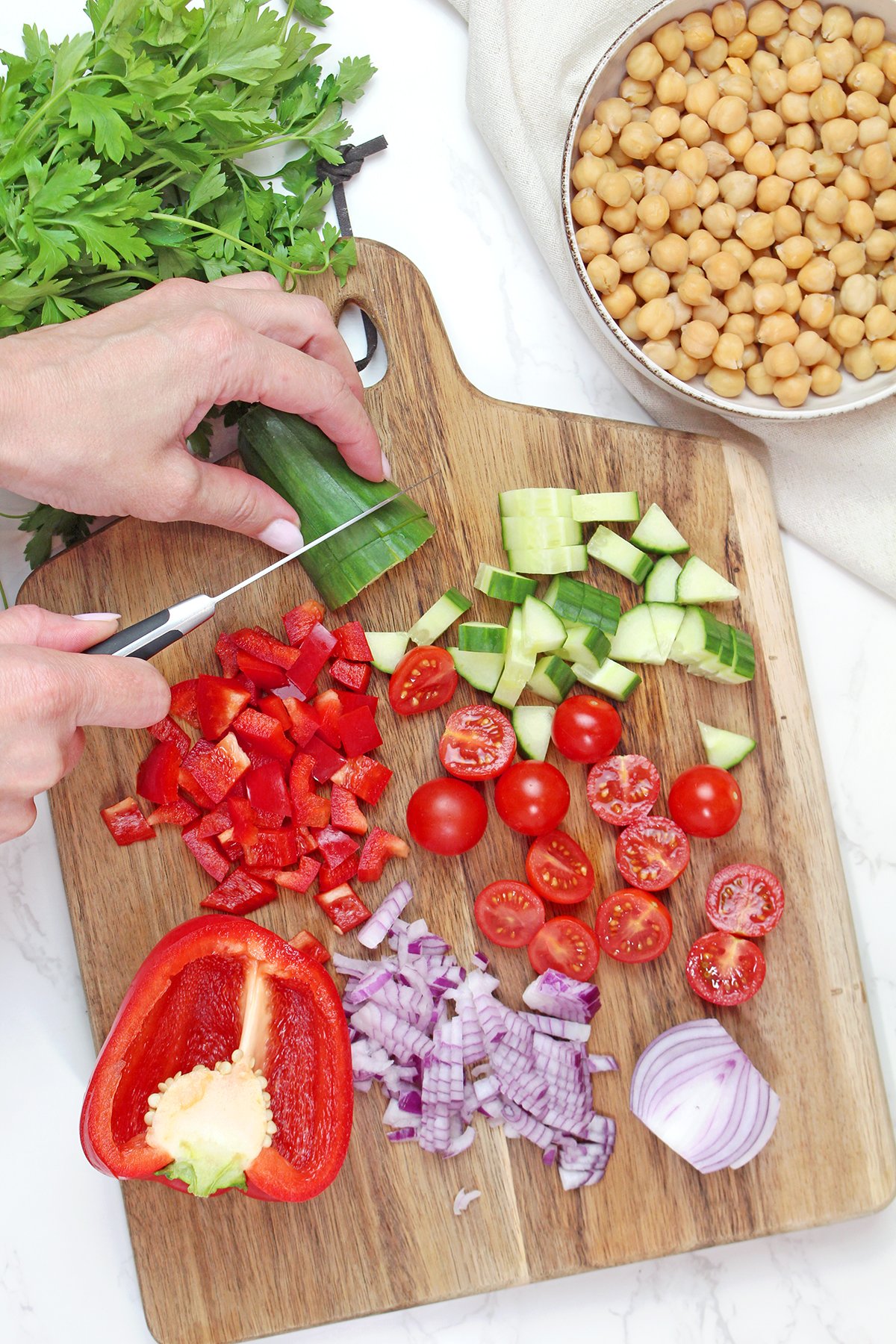 Prepped ingredients for Mediterranean chickpea salad, including chickpeas, cucumber, cherry tomatoes, bell pepper, red onion, and parsley.
