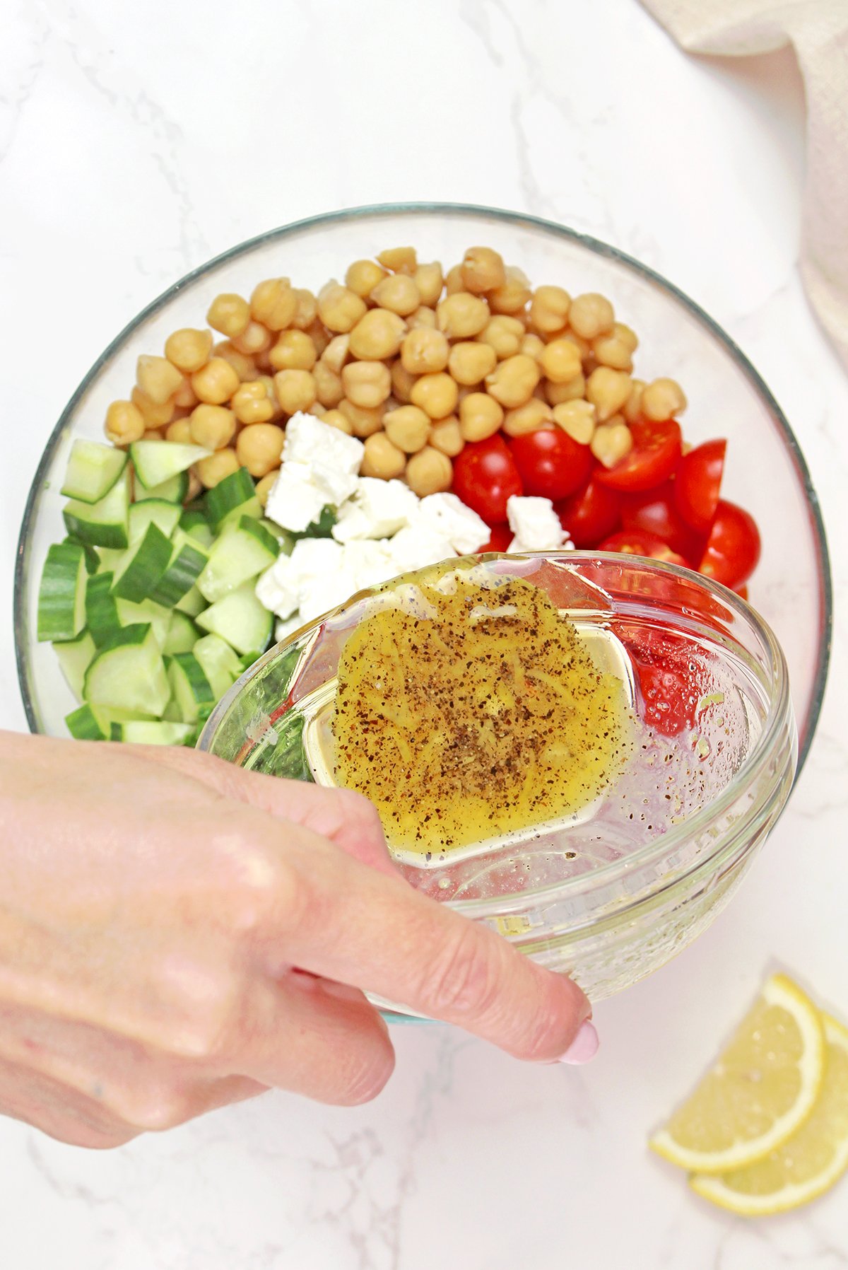 Adding lemon dressing to Mediterranean chickpea salad with chickpeas, fresh vegetables, and parsley.