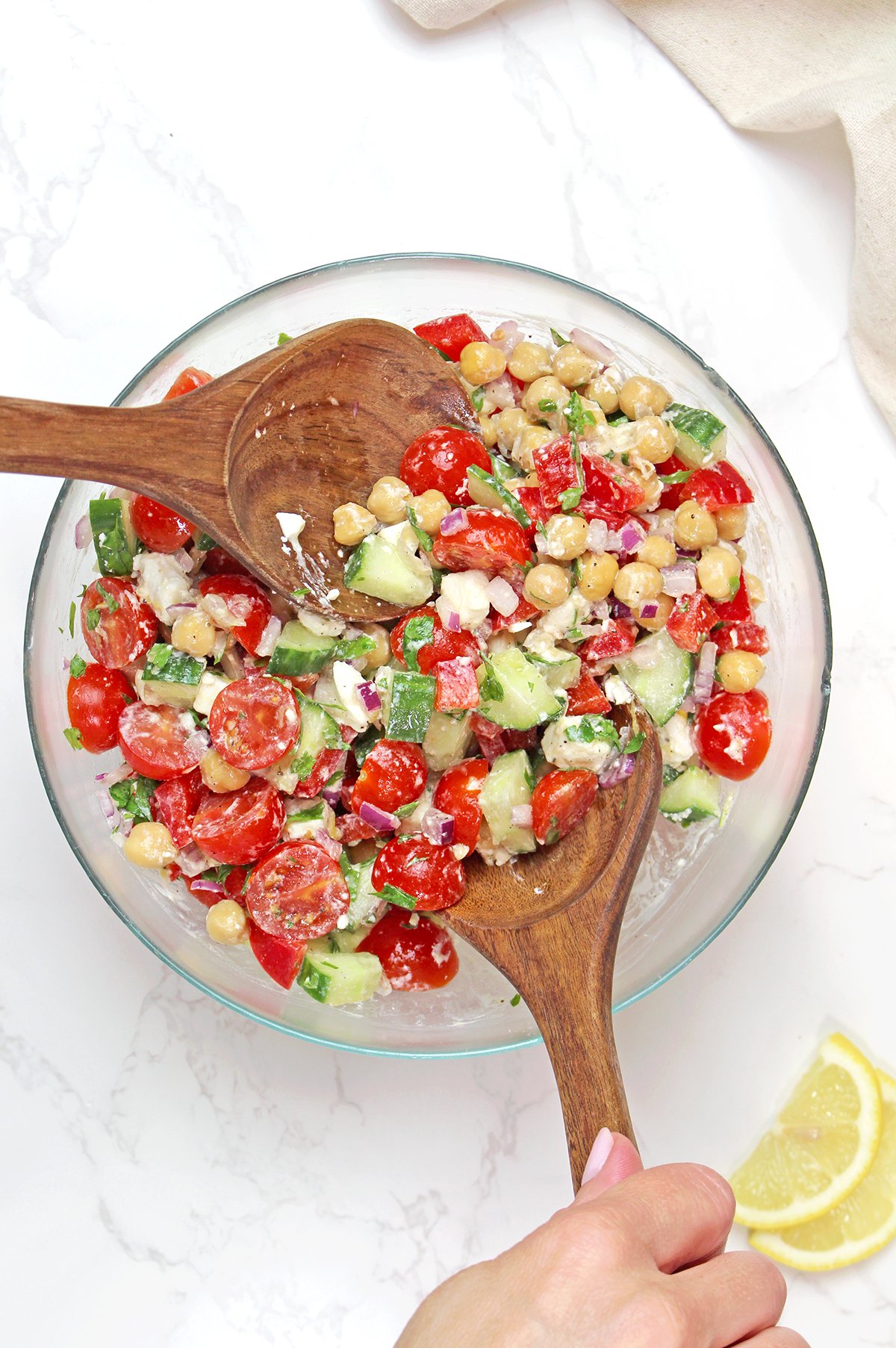 Tossing Mediterranean chickpea salad with fresh vegetables, feta cheese, and lemon dressing.