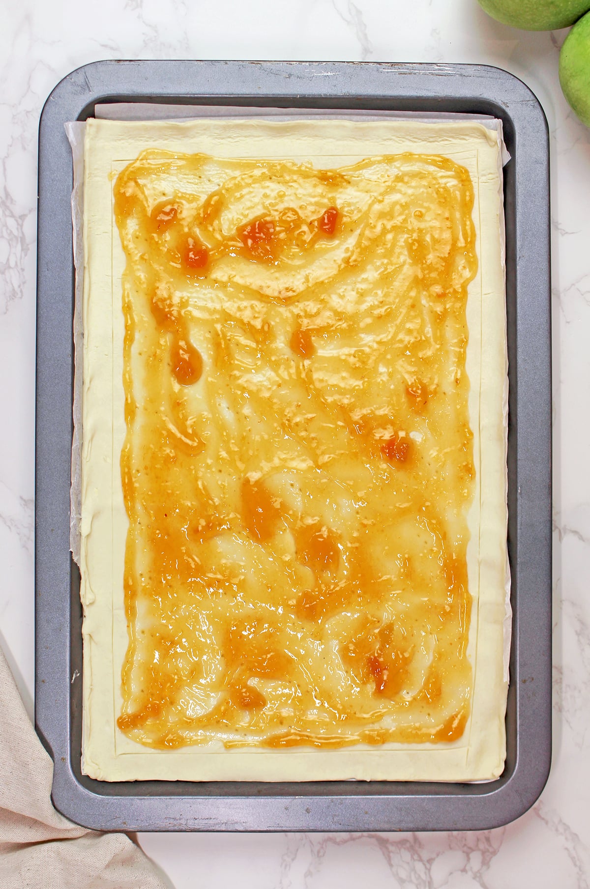Spreading apricot jam over puff pastry for an easy puff pastry apple tart.