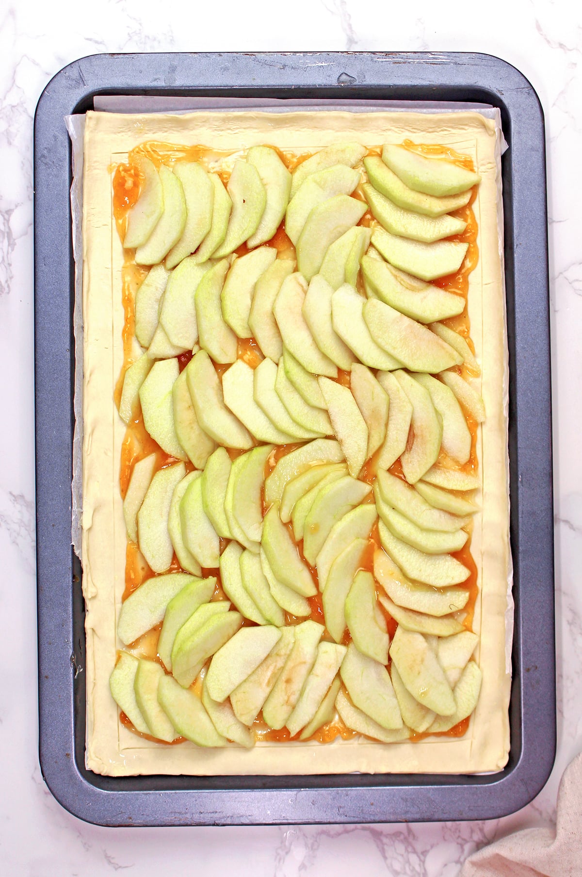 Sliced apples arranged over apricot jam for an easy puff pastry apple tart.