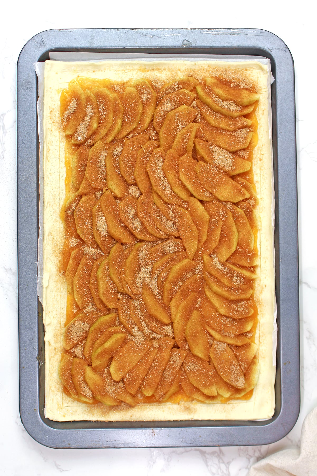 Sprinkling cinnamon sugar over sliced apples for an easy puff pastry apple tart.