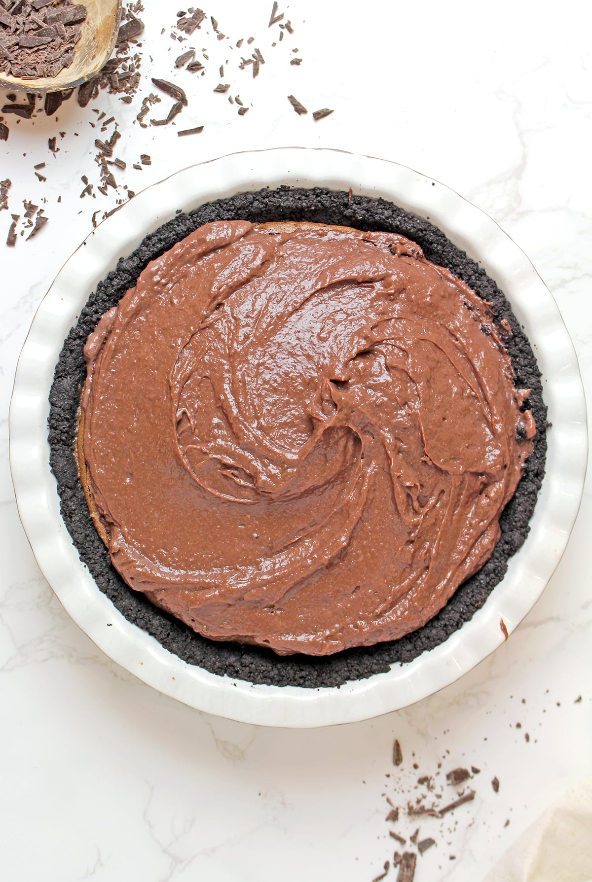 Spreading a smooth chocolate pudding layer over the cooled brownie layer and Oreo crust of Mississippi Mud Pie.