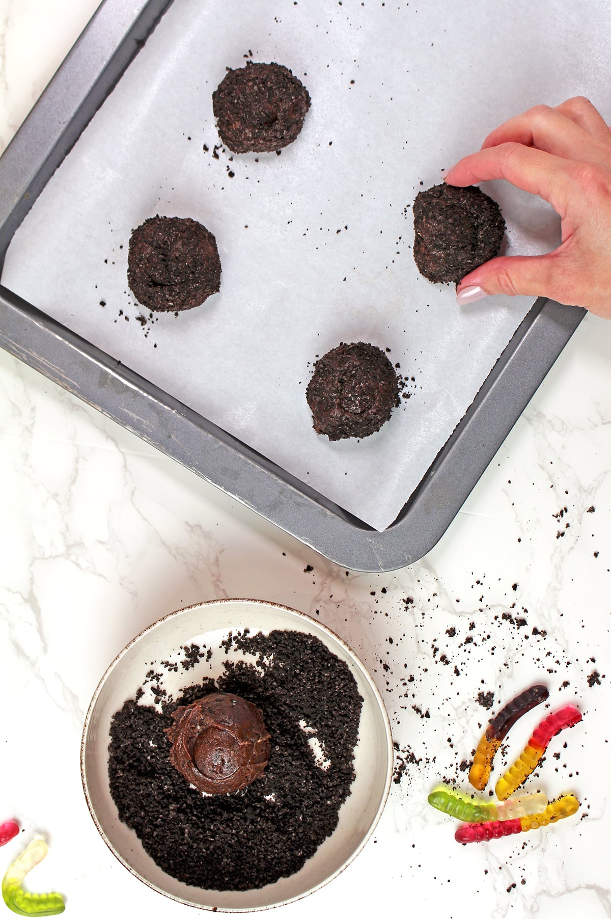 Cookie dough scoops coated in Oreo crumbs on a baking sheet.