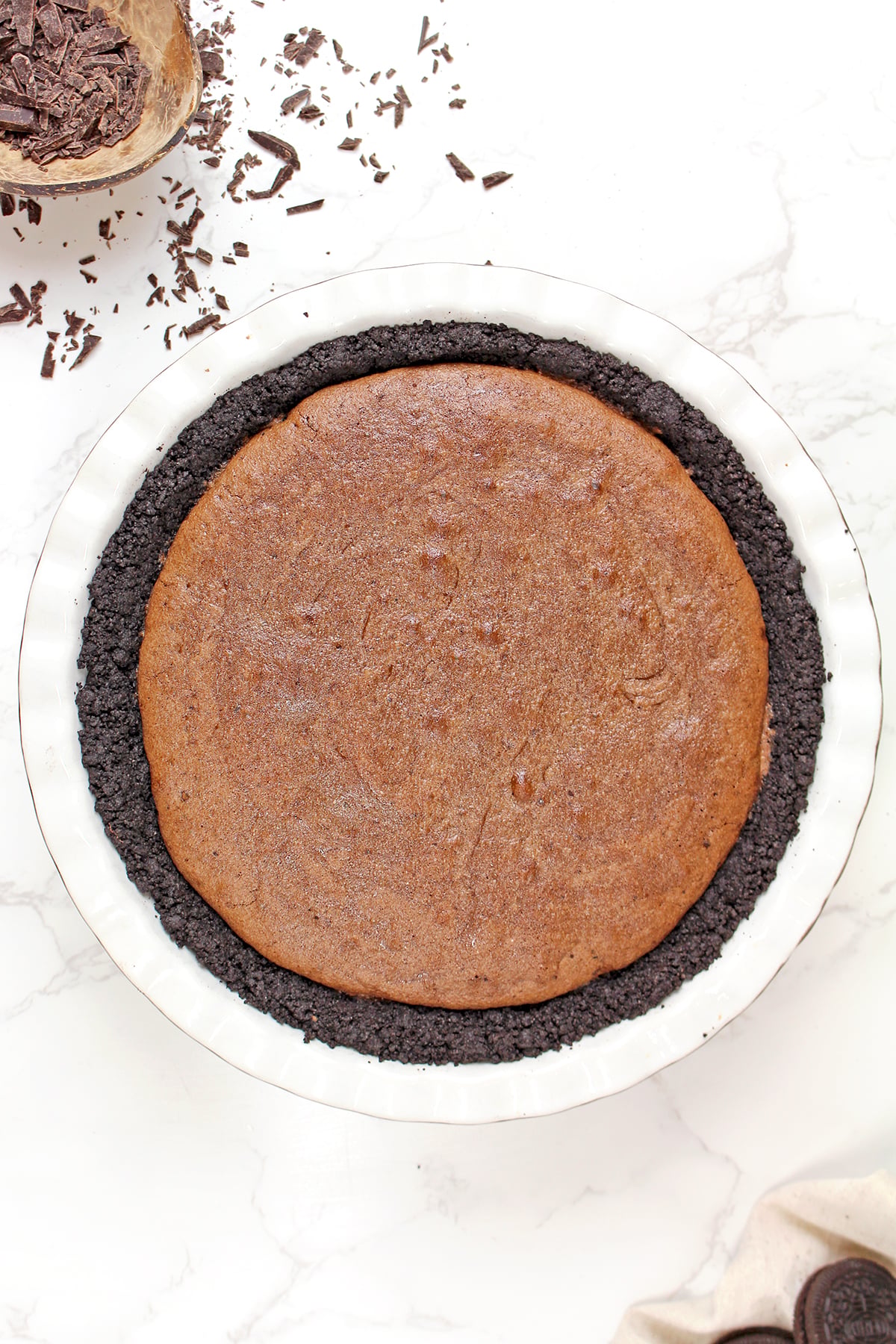 Brownie batter spread over a baked Oreo crust in a pie pan, ready to bake for Mississippi Mud Pie.